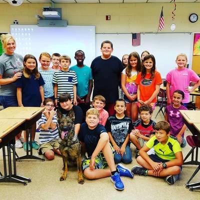 A Limitless K9 service dog and his handler posing in front of a classroom full of other students
