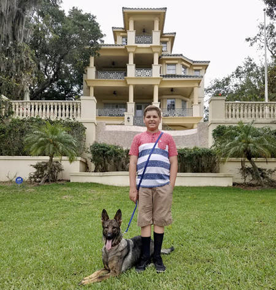 A limitless K9 service dog and his young handler in front of a large house